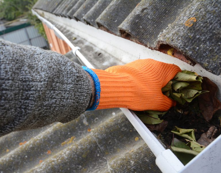 pressure washing professional in orange gloves cleaning out gutter